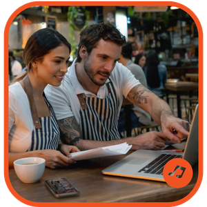 Female and male staff members in a cafe pointing at a computer screen together looking at soundtracks for business use